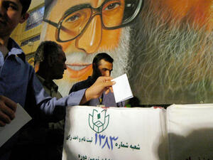 Iranian men cast their ballots beneath a poster of Ayatollah Ali Khamenei during the Iranian presidential election. (Image credit: Getty)