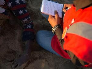 A member of the Libyan Red Crescent takes notes next to the body of a migrant on the beach in Qasr al-Garabulli, west of Tripoli, on March 20, 2016. (AFP/Stringer)