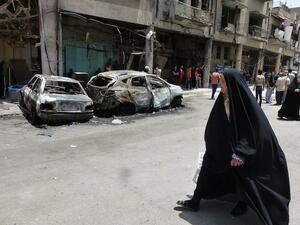An Iraqi woman walks past burnt out vehicles and damaged buildings following a car bomb explosion in Baghdad. AFP Photo