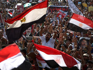 Egyptian supporters of deposed president Mohamed Morsi (portrait) wave their national flag as they attend a rally in support of the former Islamist leader outside Cairo's Rabaa al-Adawiya mosque on July 8, 2013. (Source: AFP/ MAHMUD HAMS)
