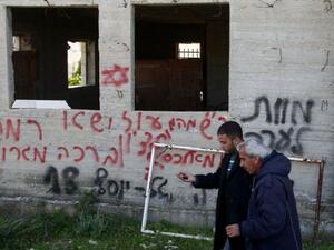 فلسطينيان يمران امام جدار عليه عبارات بالعبرية كتبها مستوطنون بالقرب من رام الله بالضفة الغربية
