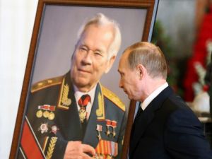 الرئيس الروسي فلاديمير بوتين يمر بالقرب من صورة للراحل ميخائيل كلاشنيكوف
