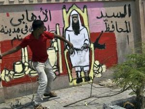 متظاهر يمسك بسلسلة حديدية أمام رسم ساخر على الجدار ضد المحافظ الجديد للاقصر
