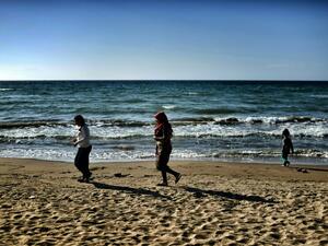 Two women walk along the beach with a child in Myrsini on April 20, 2016, a few metres away from a summer resort sheltering nearly 350 Syrian refugees. (AFP/Aris Messinis)