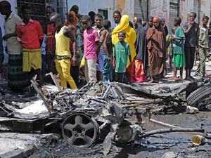 Bystanders look at the wreckage of a car bomb attack in Mogadishu on April 21, 2015. (AFP/Mohamed Abdiwahab)