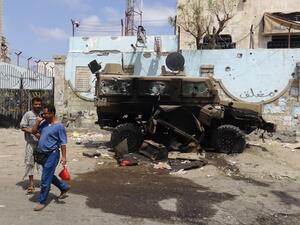 Yemeni men walk on March 13, 2016 past a charred car damaged during clashes between suspected al-Qaeda militants and policemen a day earlier, in the Mansoura residential district of the port city of Aden. (AFP/Saleh al-Obeidi)