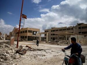 مواطن على دراجته وآخر يمر أمام مبنى مدمر في منطقة خاضعة لسيطرة المعارضة في الغوطة الشرقية بسوريا
