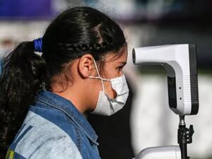 تلميذة فلسطينية في قطاع غزة تضع كمامة وتخضع لفحص حرارتها في مدرسة خاصة