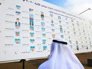 كويتي ينظر إلى لافتة انتخابية عليها أسماء المرشحين للانتخابات التشريعية