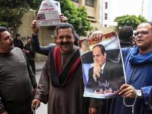 Egyptians pose for a picture with a newspaper front page and a poster of President Abdel Fattah al-Sisi (AFP)