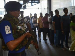 A Sri Lankan Navy personnel stands guard as Catholic devotees pray at St. Anthony's church after it was partially opened for the first time since the Easter Sunday attacks in Colombo (AFP)