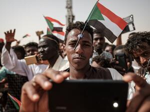 A man poses for a "selfie" photo with a cell phone while having a miniature Sudanese flag placed on his forehead with a plastic suction cap as he awaits the arrival of the deputy head of Sudan's ruling Transitional Military Council (TMC) and commander of the Rapid Support Forces (RSF) paramilitaries, during a rally in the village of Abraq, about 60 kilometers northwest of Khartoum, on June 22, 2019.  Yasuyoshi CHIBA / AFP