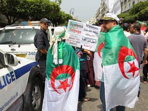 Algerian protesters, drapped in national flags, walk past a police officer during a weekly demonstration coinciding with the Algerian independence day in the capital Algiers  (AFP)