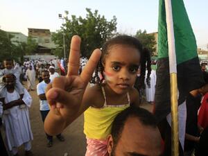 A Sudanese girl wearing facepaint on her cheeks depicting the national flag flashes the victory gesture while seated on the shoulders of a man as people celebrate after protest leaders struck a deal with the ruling generals on a new governing body, in the capital Khartoum's eastern district of Burri  (AFP)