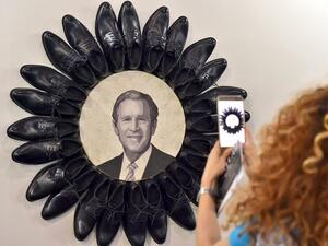 A visitor takes a picture of George W. Bush surrounded by black shoes during the opening of the Beirut Art Fair  (Twitter)