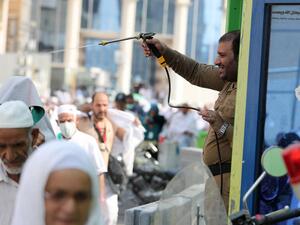 A Saudi policeman spays Muslim pilgrims with water to cool them off near the Grand Mosque (Karim Sahib/AFP)