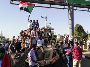 Sudanese protesters wave a national flag and flash the victory sign as they sit atop a military vehicle next to soldiers near the capital Khartoum's military headquarters on April 7, 2019. (AFP)