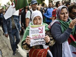 An elderly Algerian protester holds up a sign reading in Arabic "no to French guardianship, to Russian mandate, to US intervention; its excellency, the People, is master" as she marches with others draped in the national flag march during the 36th consecutive Friday anti-government demonstrations in the capital Algiers, on October 25, 2019. (RYAD KRAMDI / AFP)