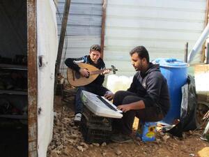 Two young men play instruments together in Azraq camp. The photo was part of an exhibition depicting teenage refugees’ aspirations and realities (Photo courtesy of Plan International)