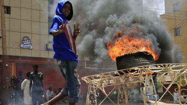 A Sudanese protester gestures as he walks past a burning tyre near Khartoum's army headquarters on June 3, 2019 after security forces broke up a weeks-long sit-in. (AFP)
