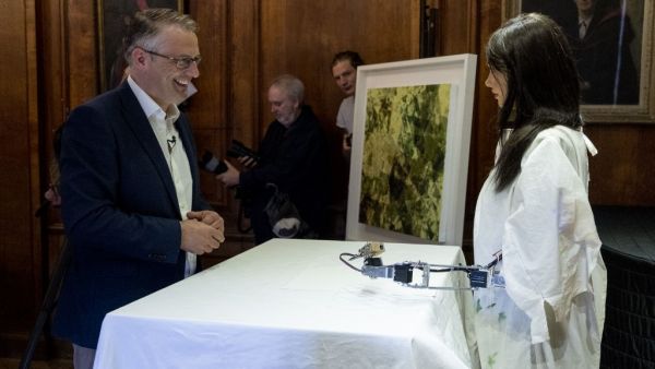 Gallery owner and creator Aidan Meller (L) talks to Ai-Da the AI humanoid robot artist (R) as it draws a portrait of him during a demonstration at a launch event for its first solo exhibition in Oxford on June 5, 2019. (Niklas HALLE'N / AFP)