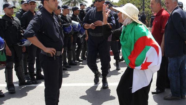 An Algerian protester wrapped with a national flag confronts riot police during the weekly Friday demonstration in the capital Algiers on June 21, 2019. (AFP)