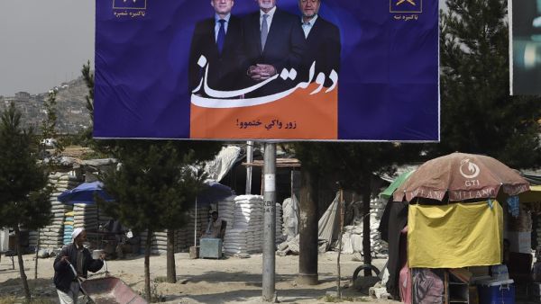 A local residents pushes a wheelbarrow past a billboard with a poster of Afghan presidential candidate and incumbent President of Afghanistan Ashraf Ghani (C) is seen during the first day of the presidential election campaign in Kabul (AFP)