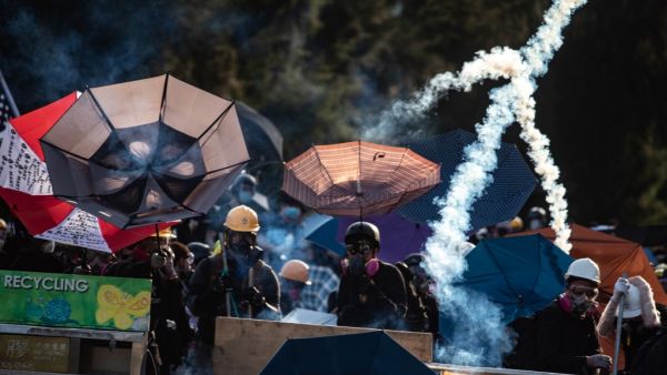 Protesters stand amid tear gas fired by the police in Tai Po district during a general strike in Hong Kong (AFP)