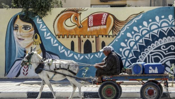 Palestinians ride a donkey cart past a mural along a street in Rafah, in the southern Gaza Strip, on September 25, 2019. SAID KHATIB / AFP
