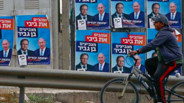 A Palestinian rides his bicycle past electoral campaign posters depicting Israeli Prime Minister Benjamin Netanyahu (right) and far-right politician Itamar Ben Gvir in the West Bank. HAZEM BADER/AFP