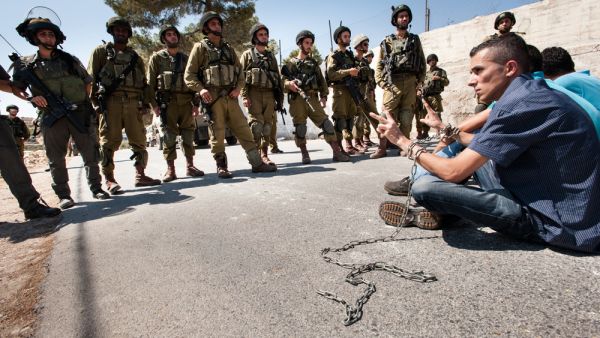 Palestinians in chains symbolizing solidarity with prisoners in Israeli jails face soldiers during a protest in Al Ma'sara, West Bank. (Shutterstock/ File Photo)