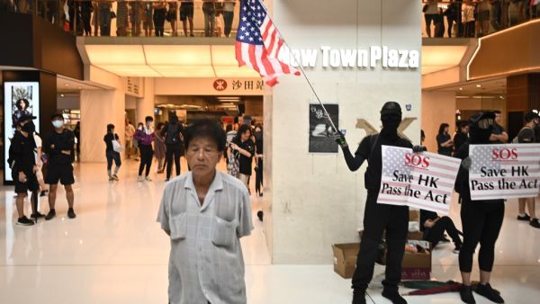 A man (L) walks past a person waving the US flag and holding a sign to rally for the US Congress to pass the Hong Kong Human Rights and Democracy Act, during a flash mob rally inside a shopping mall in the Sha Tin district in Hong Kong on October 13, 2019. (AFP/ File Photo)