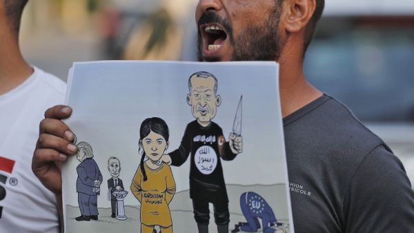 A man shouts slogans while holding up a sign showing a cartoon depicting current Turkish President Recep Tayyip Erdogan dressed in an Islamic State (IS) group uniform showing the group's logo and holding up a knife next to a woman dressed in an orange jumpsuit reading "Kurdistan"  (AFP)