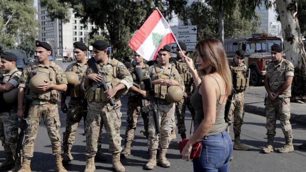 A Lebanese woman waves a national flag in front of soldiers standing guard on a main road in the eastern outskirts of the capital Beirut on October 22, 2019. Lebanese protesters gathered for a sixth consecutive day today, keeping the country on lockdown to demand new leaders despite the government's adoption of an emergency economic rescue plan.  ANWAR AMRO / AFP