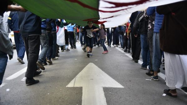 Algerian children run beneath a giant unfurled national flag carried by protesters marching during the 36th consecutive Friday anti-government demonstrations in the capital Algiers, on October 25, 2019. (RYAD KRAMDI / AFP)