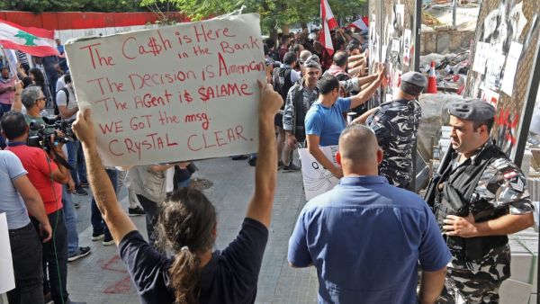 An anti-government protester holds a placard as others break down a construction barrier at the entrance of Lebanon's Central Bank during a rally at the same time of a press conference held by the bank's governor in Beirut on November 11, 2019. (AFP/ File Photo)1
