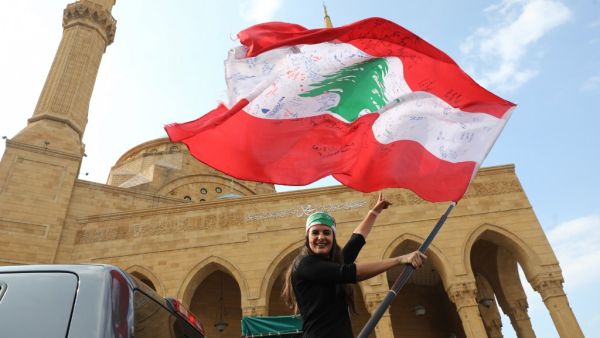 A Lebanese anti-government protester waves the national flag as she prepares to head to the south of Lebanon on a 'revolution' bus from central Beirut on November 16, 2019. ANWAR AMRO / AFP