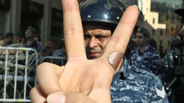 A Lebanese protester flashes the victory gesture while standing before a riot policeman at a security barrier across a road leading to the parliament headquarters during a demonstration in the capital Beirut's downtown district on November 19, 2019. An unprecedented protest movement against the ruling elite entered its second month with the country in the grip of political and economic turmoil. The leaderless pan-sectarian movement has swept the Mediterranean country since October 17, prompting the resignat