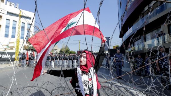 A Lebanese demonstrator waves the national flag while security forces stand by, during an anti-American protest near the US embassy in Awkar, northeast of the capital Beirut, on November 24, 2019. (ANWAR AMRO / AFP)