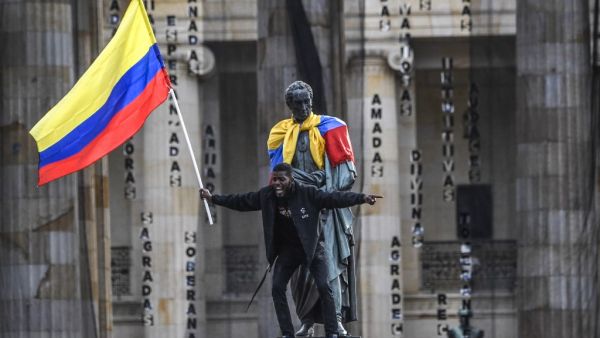 A man waves a national flag atop a statue of the Liberator Simon Bolivar during a protest against the government of Colombian President Ivan Duque in Bogota on November 27, 2019. Protest leaders in Colombia called a new general strike for Wednesday after a meeting with President Ivan Duque made no progress towards ending deadly anti-government demonstrations now in their sixth consecutive day. Juan BARRETO / AFP