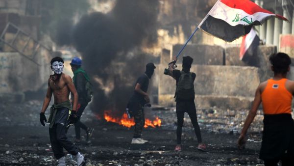 An Iraqi anti-government protester waves a national flag close to a concrete barricade amidst clashes with security forces along the capital Baghdad's Rasheed street near al-Ahrar bridge  (AFP)