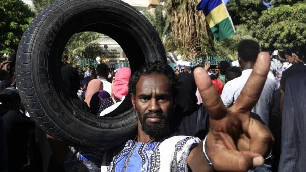 Sudanese protester flashes the victory gesture while holding a car tire on his shoulder during a demonstration in the centre of Sudan's capital Khartoum outside the prime minister's offices (AFP)