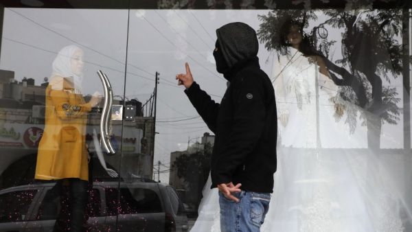 A masked member of the Palestinian Fatah political party tells a woman to close her shop in the southern West Bank city of Hebron after the party called a general strike over Israeli settlement activity in the area, on December 9, 2019. (AFP/ File Photo)