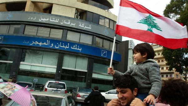 A Lebanese protester carries a child as he takes part in a rally in front of a bank in the southern city of Sidon (Saida) on December 30, 2019 to protest against nationwide imposed restrictions on dollar withdrawals and transfers abroad in an attempt to conserve dwindling foreign currency reserves. (AFP/ File Photo)