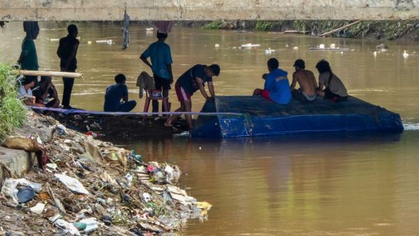 Young men wait under a concrete bridge looking to salvage valuable items carried by the currents in Jakarta on January 3, 2020, after flooding triggered by heavy rain which started on New Year's Eve hit the area. (AFP/ File Photo)