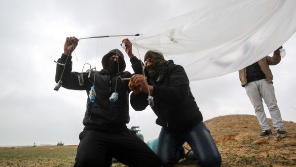 Young Palestinian men, masked in order to avoid being recognised, prepare a flammable object to be flown toward Israel, near the Israel-Gaza border east of Rafah in the southern Gaza Strip, on January 18, 2020. SAID KHATIB / AFP