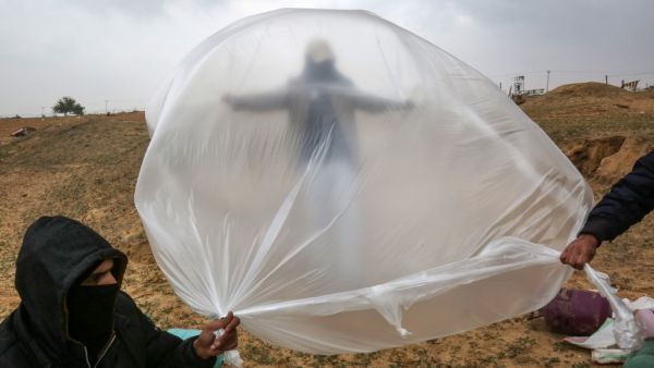Young Palestinian men, masked in order to avoid being recognised, prepare a flammable object to be flown toward Israel, near the Israel-Gaza border east of Rafah in the southern Gaza Strip, on January 18, 2020. SAID KHATIB / AFP