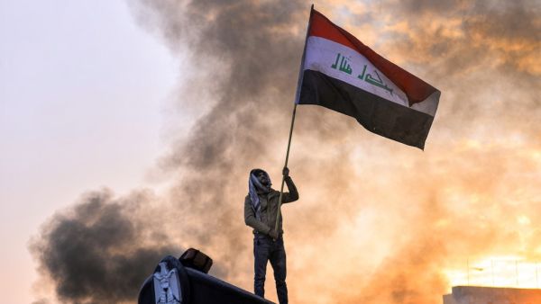An anti-government protester waves a national flag as he stands above a statue of a policeman's hat during a demonstration in the central Iraqi holy shrine city of Najaf on January 19, 2020. Haidar HAMDANI / AFP