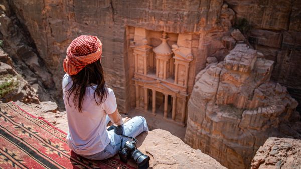 Asian woman traveler sitting on carpet viewpoint in Petra ancient city looking at the Treasury or Al-khazneh, famous travel destination of Jordan and one of seven wonders. (Shutterstock/ File Photo)