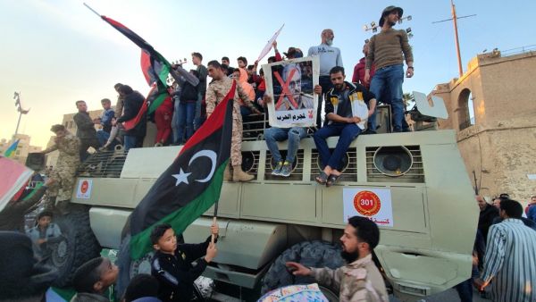 A man holds up a sign showing the face of Libyan strongman Khalifa Haftar with a red "X" above him and a caption in Arabic reading "no to the war criminal". AFP